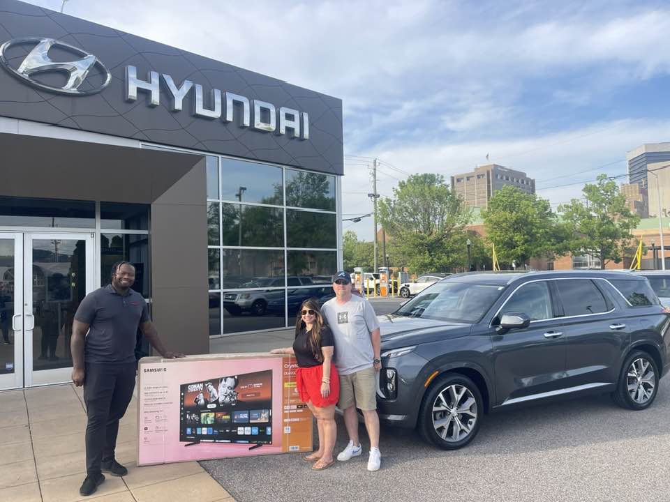 Christian Smith handing over keys to smiling customers beside their new Hyundai SUV at the dealership